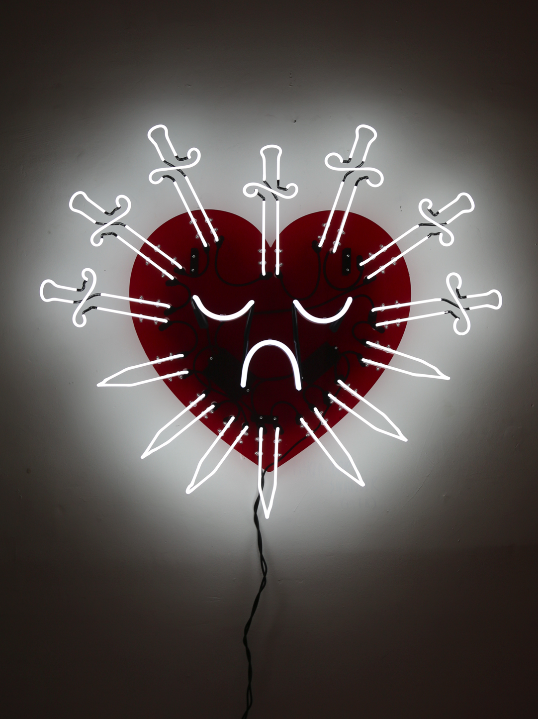 A neon sign featuring seven swords mounted to a transparent red acrylic piece cut in the shape of a heart.